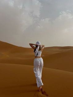 a woman standing in the desert with her arms behind her head, looking up into the sky