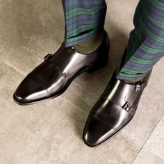 a man in plaid pants and black shoes is standing on the floor with his legs crossed