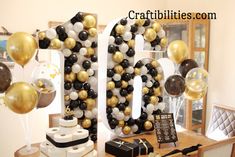 a table topped with lots of black and gold balloons next to a sign that says 10