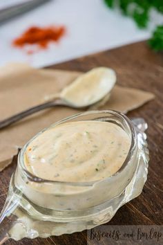 a small glass bowl filled with dressing on top of a wooden table next to a spoon