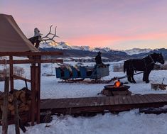 a horse pulling a sleigh in the snow next to a fire pit and mountains