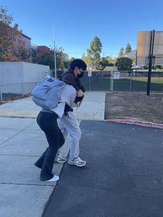 two people are standing on the sidewalk and one person is holding a back pack in front of them