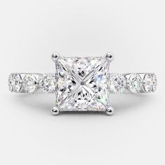 a princess cut diamond engagement ring with three stones on the band and side stones around the band