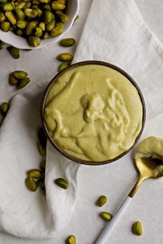 a bowl filled with green sauce next to a spoon and some pistachios