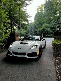 a white sports car is parked on the side of the road in front of some trees