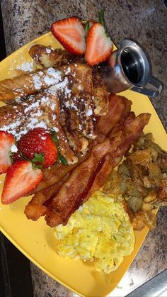 a yellow plate topped with bacon, eggs and strawberries