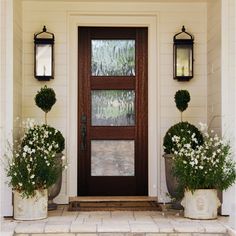 two planters with flowers are on the front step of a house, next to an entry door