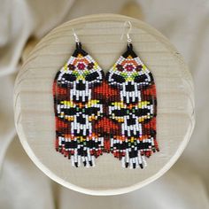 a pair of beaded owl earrings sitting on top of a wooden hoop hanging from a white wall