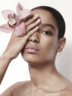 a woman is holding her hand to her face with a flower in front of her eye