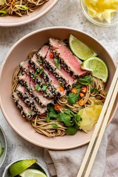 two bowls filled with noodles, meat and vegetables on top of a white tablecloth