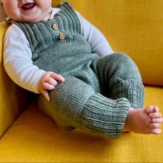 a baby sitting on a yellow couch with his hands in his pockets and smiling at the camera