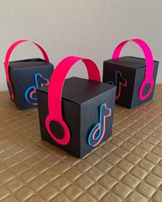 three black boxes with pink and blue headphones on them sitting on a brown table