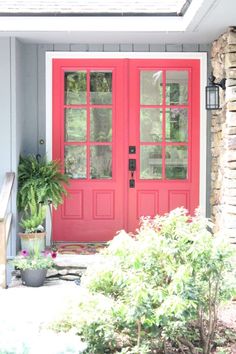 a red front door with two sidelights and potted plants