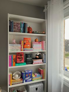 a bookshelf filled with lots of books next to a window