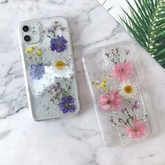 two iphone cases with flowers on them sitting on a marble table next to a plant