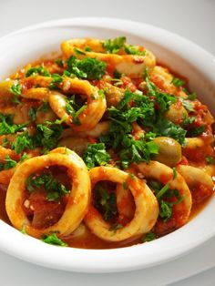 a white bowl filled with pasta covered in sauce and garnished with parsley