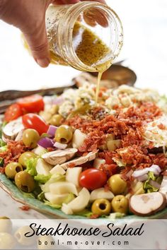 someone pouring dressing onto a salad with olives, tomatoes, and other vegetables on it