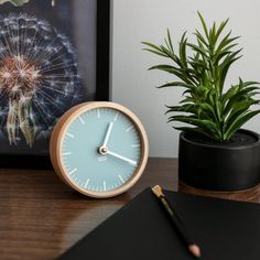 a clock sitting on top of a wooden table next to a plant and a notebook