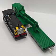 a toy train is on the tracks next to a green and yellow track with a tractor attached