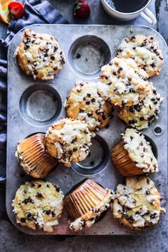 orange chocolate chip muffins in a muffin tin next to a cup of coffee