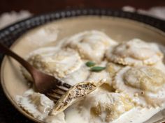 a plate filled with dumplings covered in white sauce and a wooden fork sticking out of it