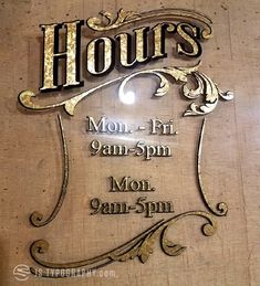 a sign that says hours on the side of a building with an ornate design and gold lettering