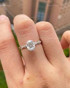 a person's hand with a diamond ring on top of their finger, in front of a building