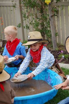 several children in cowboy hats are sitting on the grass and playing with a water table