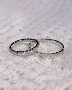 two wedding rings sitting on top of a white blanket next to each other with diamonds