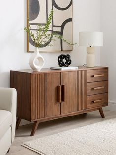 a living room with a white chair and a wooden cabinet in front of a painting on the wall