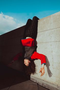 a man is upside down on the ground with his hands in the air while standing next to a concrete wall