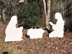 three cutouts of the nativity scene in front of a wooden fence and tree