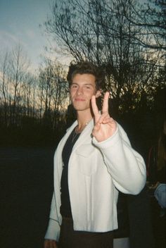 a young man making the peace sign with his hand while standing in front of trees