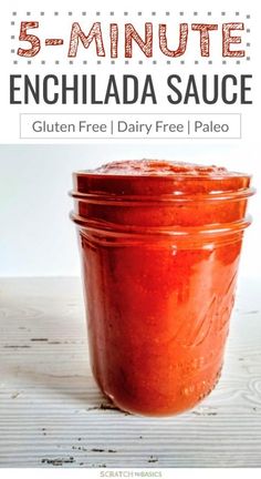 a jar filled with red sauce sitting on top of a wooden table next to a white wall