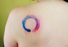 the back of a woman's shoulder with a blue and red circle tattoo on it