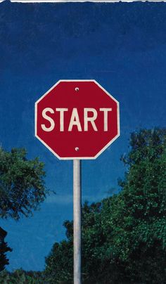 a stop sign with the word start on it in front of trees and blue sky