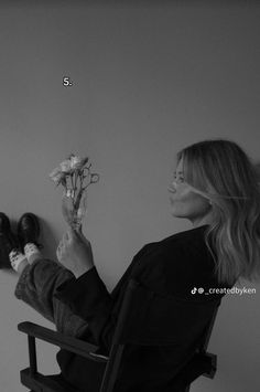 a woman sitting in a chair holding flowers and looking at the wall with her feet up