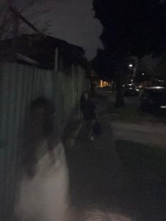 a blurry photo of people walking down the street at night time, with one person holding an umbrella