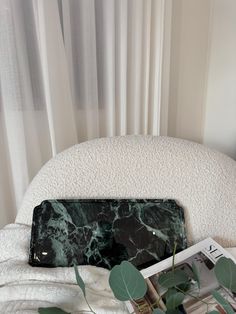 a marbled black and green purse sitting on top of a bed next to a plant