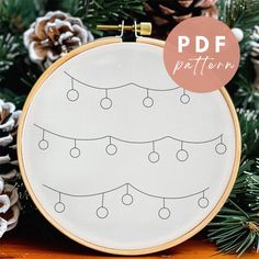 a hand embroidered christmas ornament on a wooden table with pine cones and evergreen needles