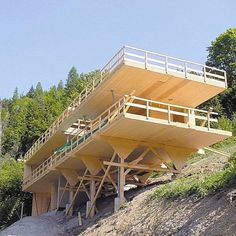 a large wooden structure sitting on top of a hill next to a lush green forest