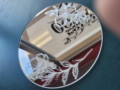 a round mirror with white flowers on the side and a person's reflection in it