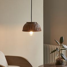 a lamp hanging over a table next to a chair and potted plant in a room