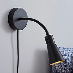 a black wall light on a white wall next to a blue and white blanket with a gold accent