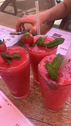 three glasses filled with red liquid sitting on top of a table next to each other