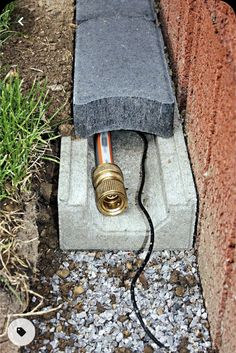 an electrical device is plugged in to a brick wall with gravel and grass around it