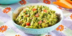 a bowl filled with guacamole sitting on top of a table next to carrots