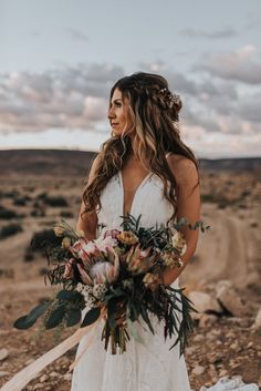 a woman standing in the desert holding a bouquet