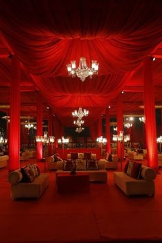 a room with couches, chandeliers and red drapes on the ceiling