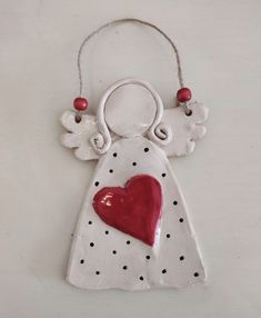 a ceramic ornament with a red heart and angel wings hanging from it's side